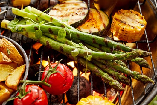 Healthy fresh vegetables grilling on a BBQ with zucchini, potato wedges, asparagus, tomato and corn on the cob in a close up view
