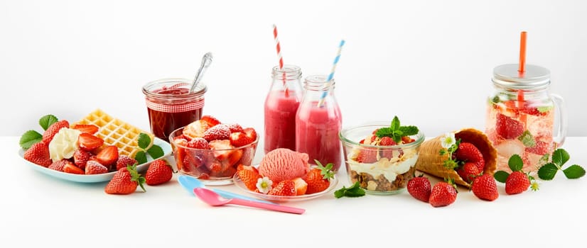 Strawberry themed panorama of fresh fruit recipes with waffles, puree, jam, salad, ice cream, muesli topped with berries and infused water over white