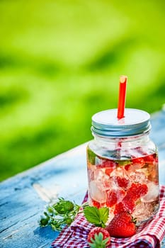 Fresh, chilled fruit and berry infused punch bowl in a glass jar with a straw on a bright outdoor table setting.