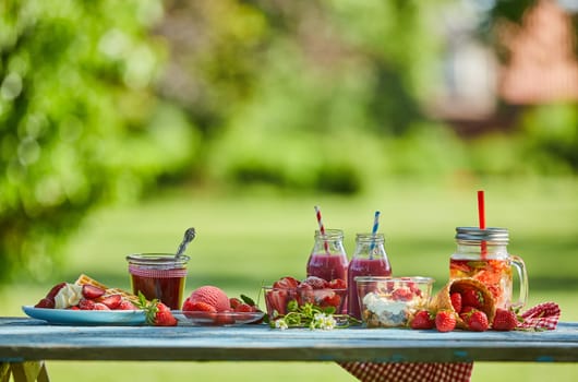 Fresh, healthy, vibrant summer berry smoothie bowl, juices and desserts picnic on a bright outdoor table setting.