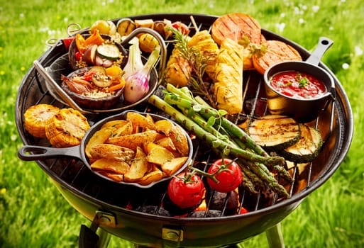 Large assortment of fresh vegetables grilling on a Portable BBQ outdoors on green grass in summer over the hot coals