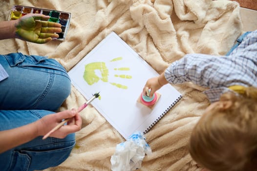 Artistic activity where a child and parent express creativity together by painting, symbolizing love and quality time shared during early childhood and family moments.