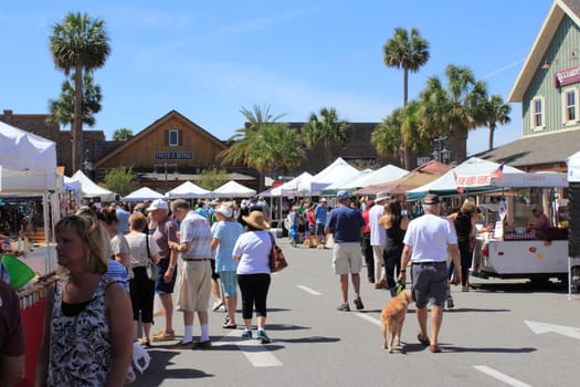 The Villages, FL, USA -April 1, 2017: People shop at a farmer’s market. Street market shops under canopies sell to shoppers on a sunny day. People at farmer’s market shops near Paddock Square.