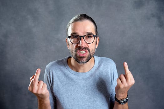 young man in front of gray background showing middle finger