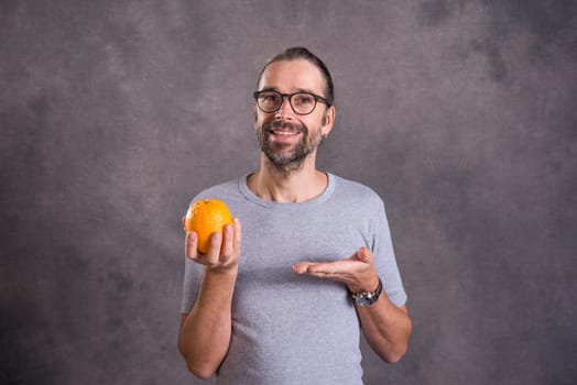 long haired young man with orange in front of gray background