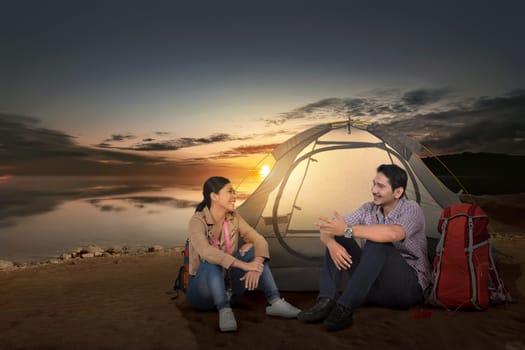 Happy asian couple traveler with tent enjoying sunset time beside the lake