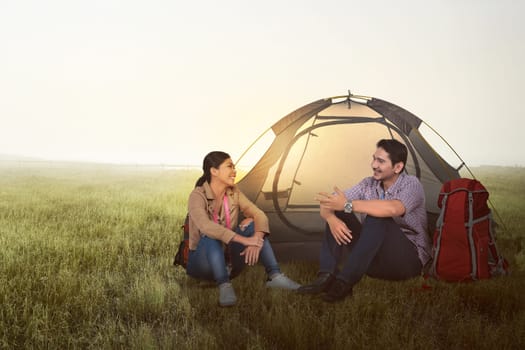 Smiling asian couple camping with backpack and tent on the meadow field