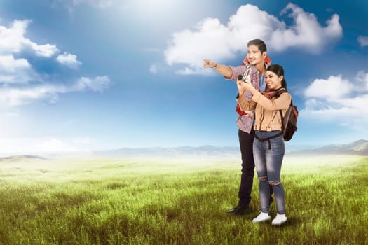 Happy asian couple tourist look around and taking a photos on the meadow field