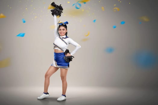 Happy asian cheerleader with pom-poms in her hands over confetti background