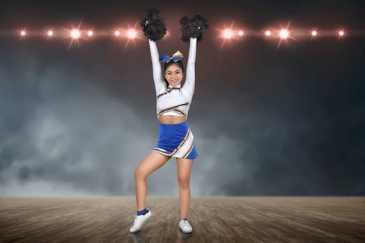 Smiling asian cheerleader perform with pom-poms with spotlights on background
