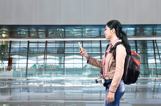 Smiling asian tourist woman with backpack using cellphone on the airport
