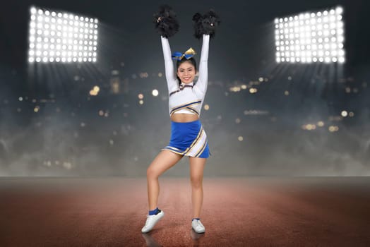 Pretty asian cheerleader with hands holding pom-poms in the air on the stadium