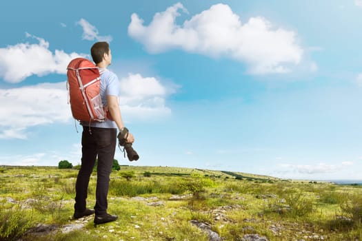 Attractive asian traveler man with backpack and camera on the meadow