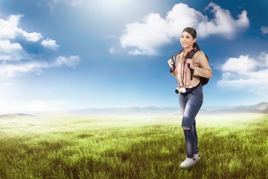 Beautiful asian traveler woman with camera and backpack relaxing on the meadow