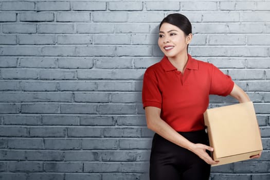 Smiling asian delivery woman carrying the parcel with wall background
