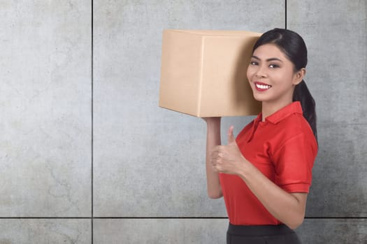 Smiling asian courier woman bring the parcel against gray wall background