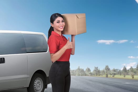 Pretty asian delivery woman standing with the package against van on the background