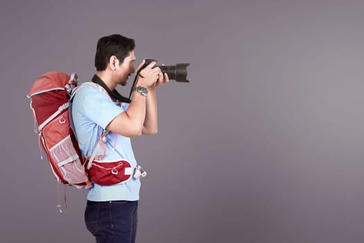 Handsome asian photographer man taking a photos with camera over colored background