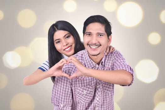 Romantic asian couple  in love make a heart shape with their hands against blur light background