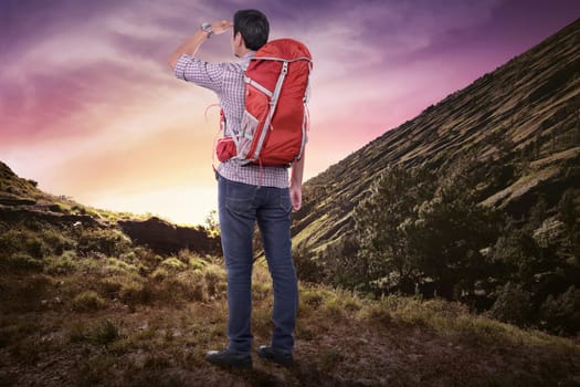 Back view of asian tourist man with backpack looking at scenery on the mountain