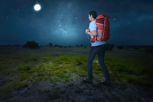 Attractive asian traveler with backpack walking on the field at night
