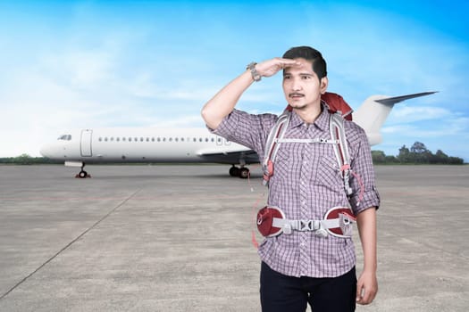 Handsome asian traveler man with backpack looking around on the plane runway