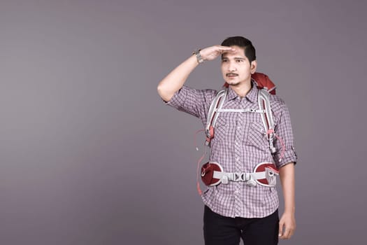 Excited asian tourist with backpack looking around over wall background