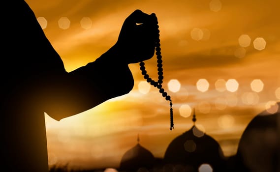 Silhouette of muslim man praying with prayer beads during sunset background
