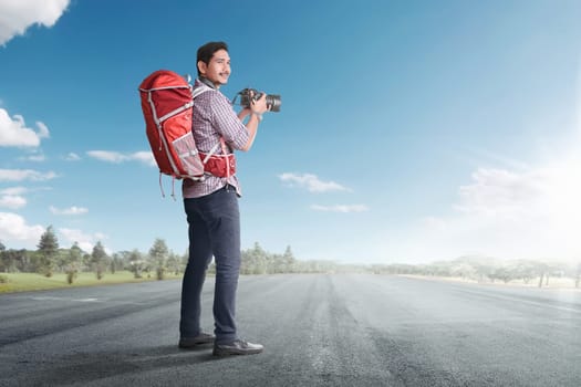 Young asian tourist with backpack and camera on the empty road