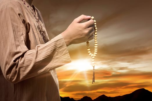 Muslim man praying with prayer beads during sunset background