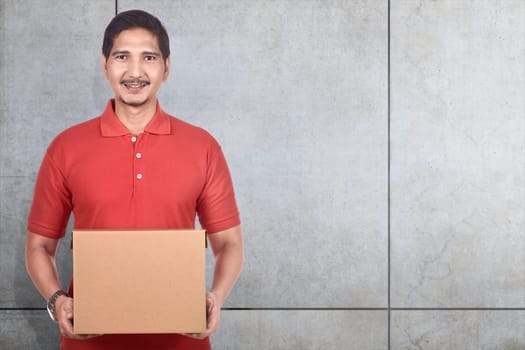 Young asian delivery man holding cardboard boxes over gray wall background