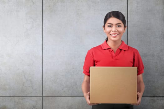 Pretty asian woman courier with cardboard box over gray wall background