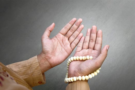 Muslim man praying with prayer beads over gray background