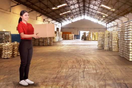 Joyful asian female courier holding cardboard box on the warehouse