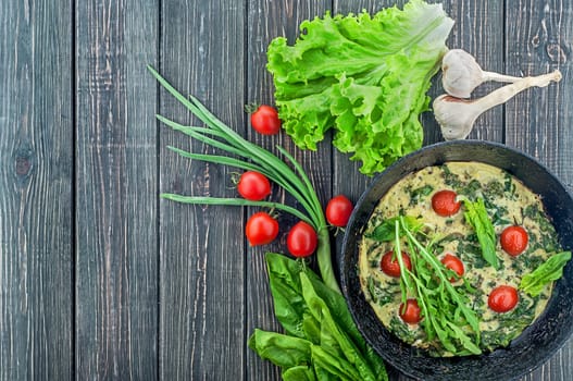 Fritatta with tomatoes and ingredients. An old frying pan on a wooden table. View from above. Free space.