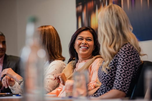 Two businesswomen talking while sitting down at a conference table. Waiting for the meeting to start.