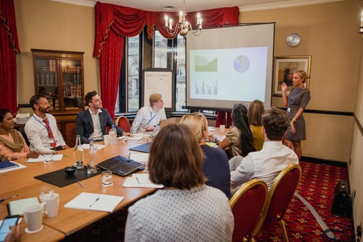 Rear view of a large group of people lookig towards a businesswoman giving a presentation within a meeting.