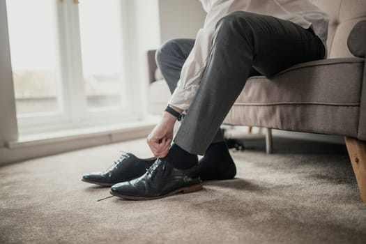 Unrecognisable person adult male sitting on a sofa in a domestic room tying his shoelaces.