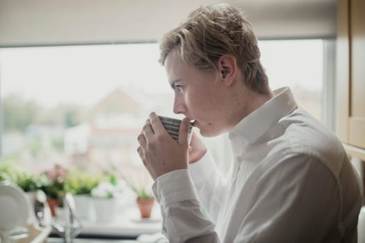 Close-up, side view of a young adult male drinking a cup of tea. The young adult is wearing formal clothes.