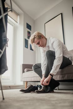 Low angle view of a young businessman sitting on the sofa tying his shoe laces.