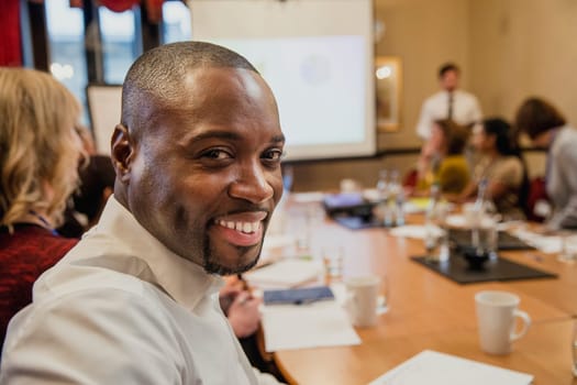 Mid-adult businessman turning in his seat, looking at the camera and smiling for a headshot.
