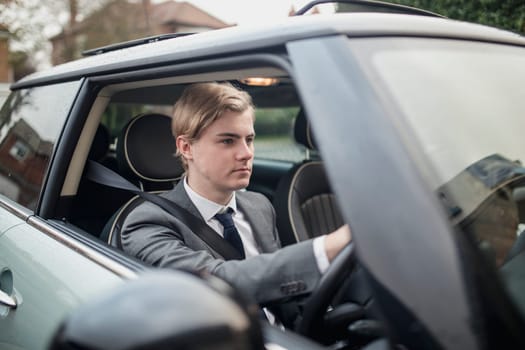 Young adult businessman concentrating while driving his car off the driveway to go to work.