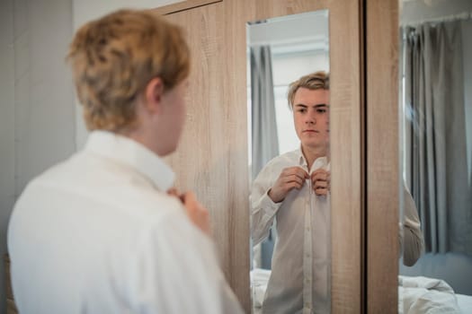 Rear view of a young adult male getting dresses infront of the mirror. Putting on a button down shirt for work.