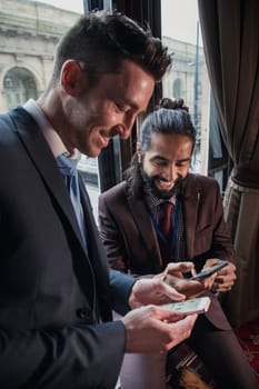 Side view of two businessmen on their smart phones swaping contact details. Both smiling and laughing.