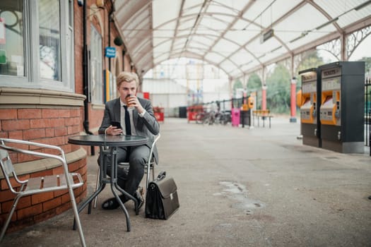 Young businessman drinking coffee at the trainstation while waitng to go to work.