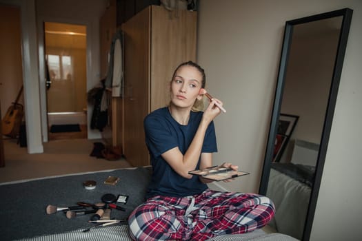 Front view of a young female adult applying make-up during her morning routine.