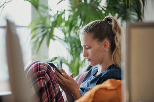 Side view of a young female adult sitting, relaxing, using her mobile phone.