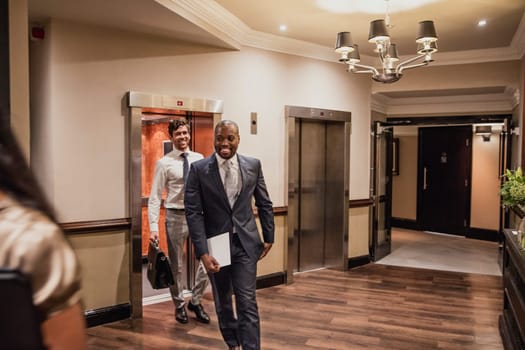 Front view of two businessmen walking from the lift at the convention centre to go on a lunch break.