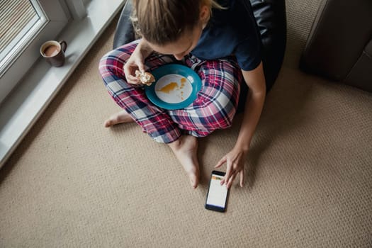 Aerial view of a young female adult sitting and eating breakfast and scrolling though social media in the morning