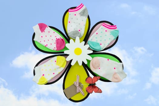 Colorful presentation of a set baby socks on a summer flower with natural sky background. Butterfly with tag. Copy space.